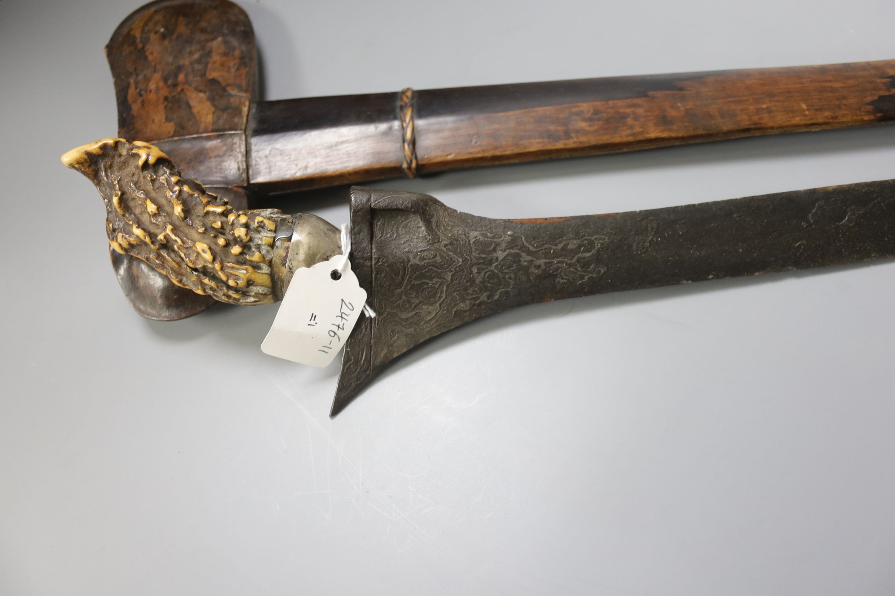 An Indonesian dagger kris, 19th century, earlier swollen black and silver-coloured watered blade, natural staghorn handle, silver cup, wooden scabbard, blade 38cms.